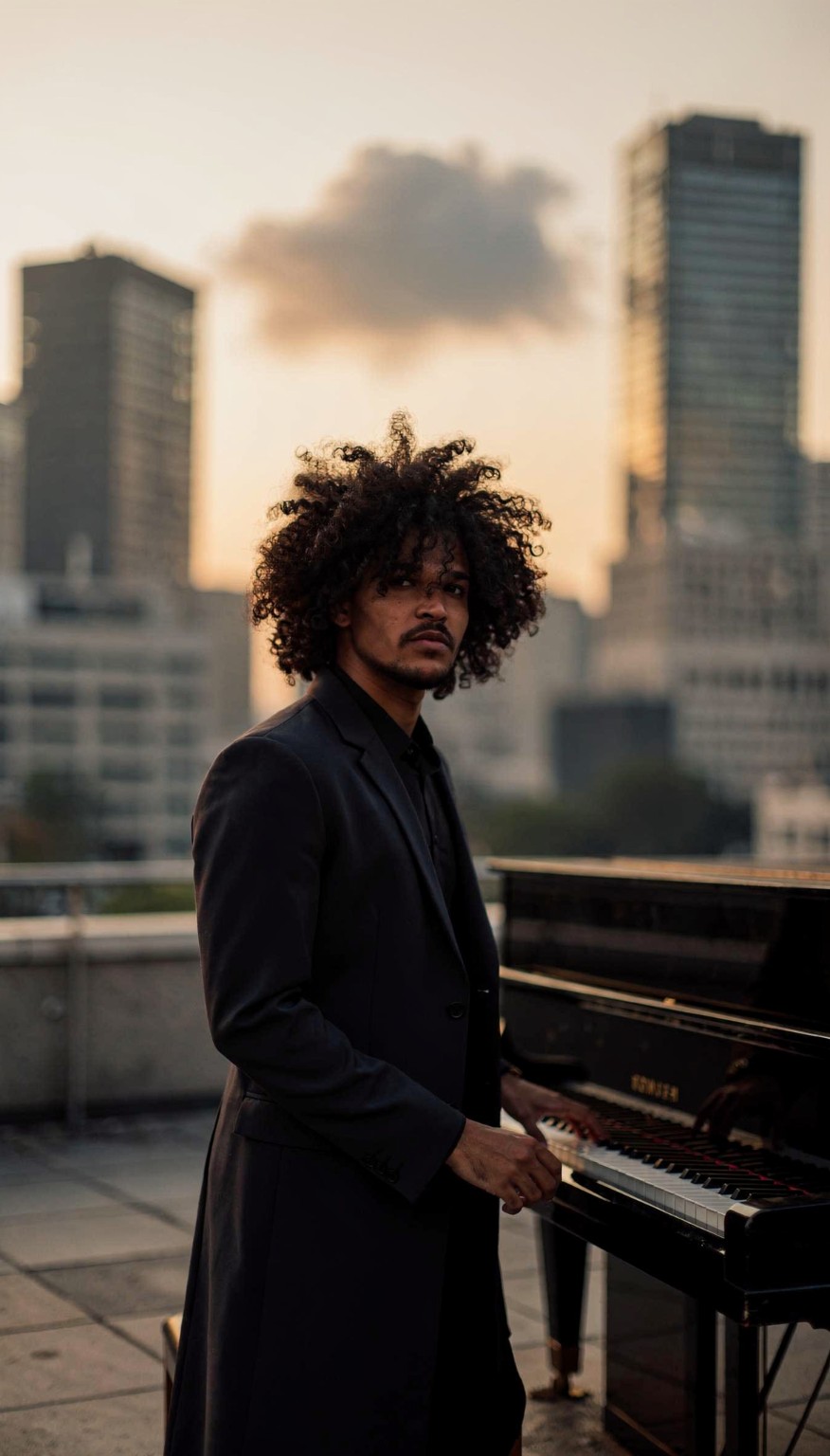 Gabriel at a piano on a rooftop with the city behind him