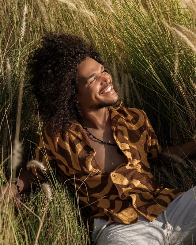 Gabriel Oramas smiling, sitting back in tall grass in warm golden light