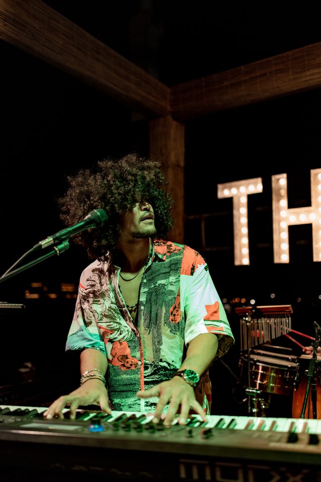 Gabriel Oramas performing on stage, playing keyboard and singing into a microphone under green stage lights
